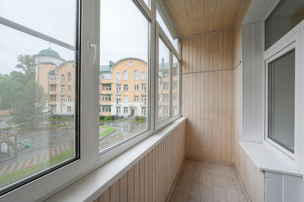 bright balcony with light wood paneling and large windows showcasing a wet cityscape with a building and playground